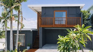 Una moderna casa a due piani con un balcone, una scala e vegetazione circostante.