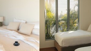 Una camera d'albergo con un letto, una finestra che si affaccia su palme e un comodino con una lampada.