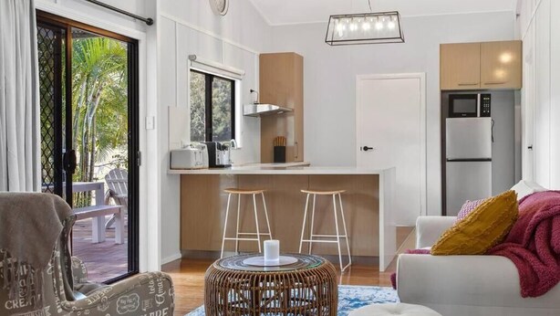 Un salon moderne avec un canapé, un pouf et une table basse ronde. Il y a également un coin cuisine équipé d’un four à micro-ondes et d’un réfrigérateur.