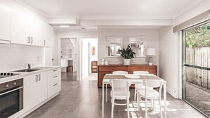 Une cuisine moderne avec des meubles blancs, un coin repas comprenant une table et des chaises, et une grande fenêtre donnant sur l’extérieur.