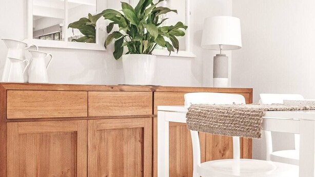 Une cuisine moderne avec des meubles en bois, un plan de travail blanc, une plante en pot, une chaise blanche et une table avec une lampe.