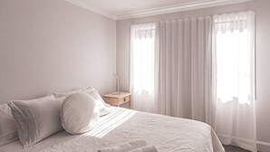 Une chambre à coucher avec un grand lit, une table de chevet et une fenêtre ornée de rideaux légers.