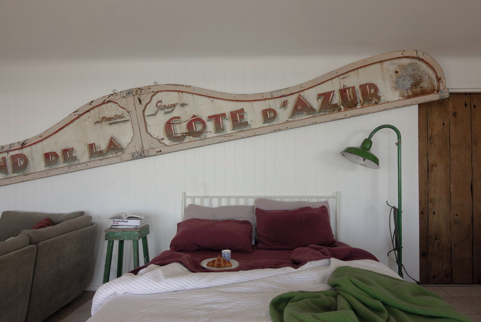 Une chambre à coucher avec un lit, des oreillers, une table de chevet avec un livre, une lampe et un panneau rustique au-dessus du lit.