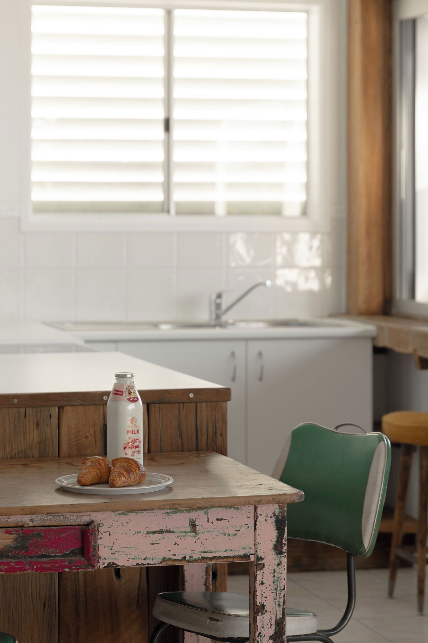 A kitchen with a wooden table, a green chair, and a bottle of milk.