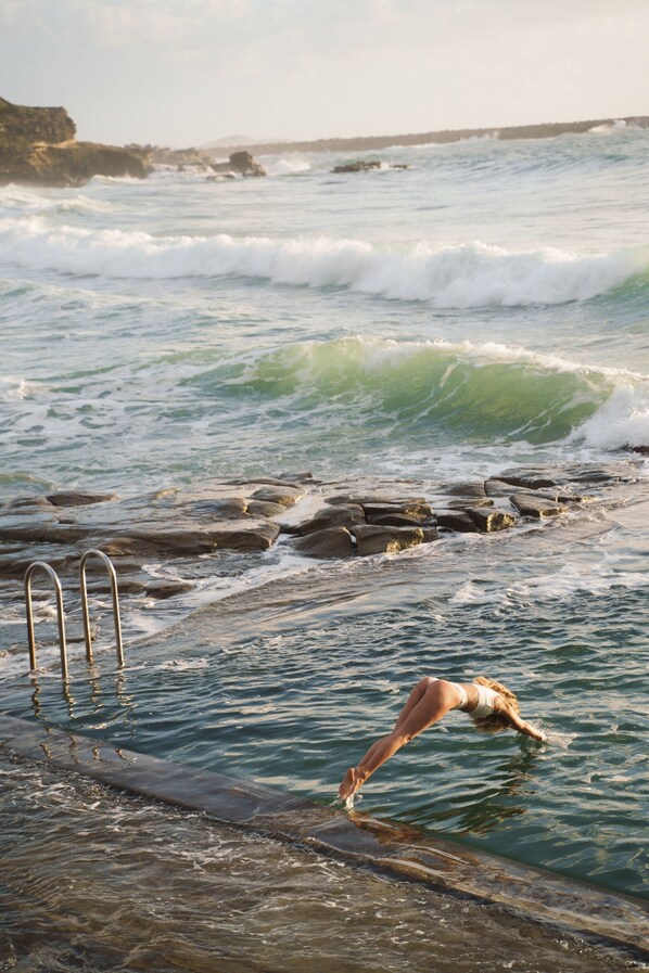 A rocky shoreline with waves crashing onto the rocks and a metal ladder leading into the water.