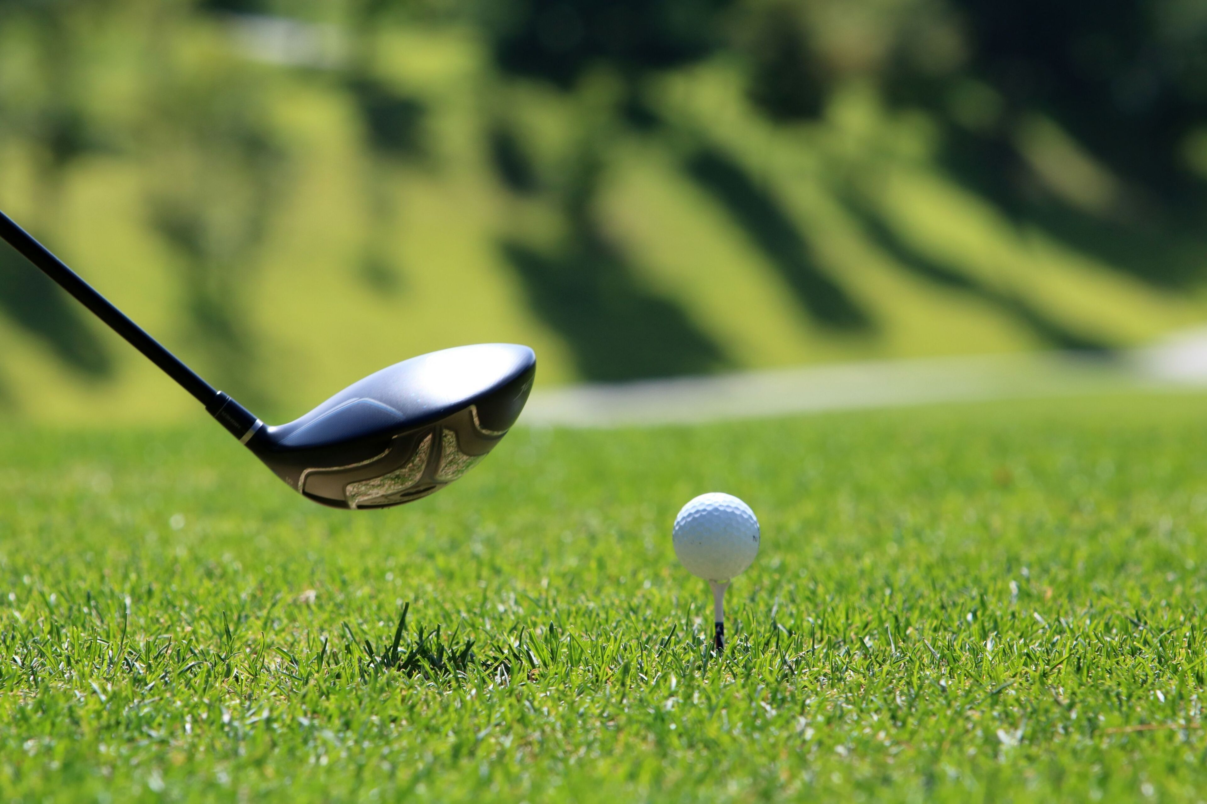 Un palo de golf en pleno balanceo, con una pelota de golf sobre un tee en un campo de césped.