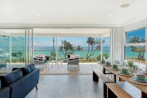 Een moderne eetruimte met uitzicht op zee, een houten terras en een glazen balkon.