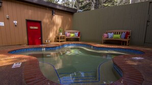 Area idromassaggio con porta rossa per la sauna, due panche di legno con cuscini colorati e una piscina piastrellata.