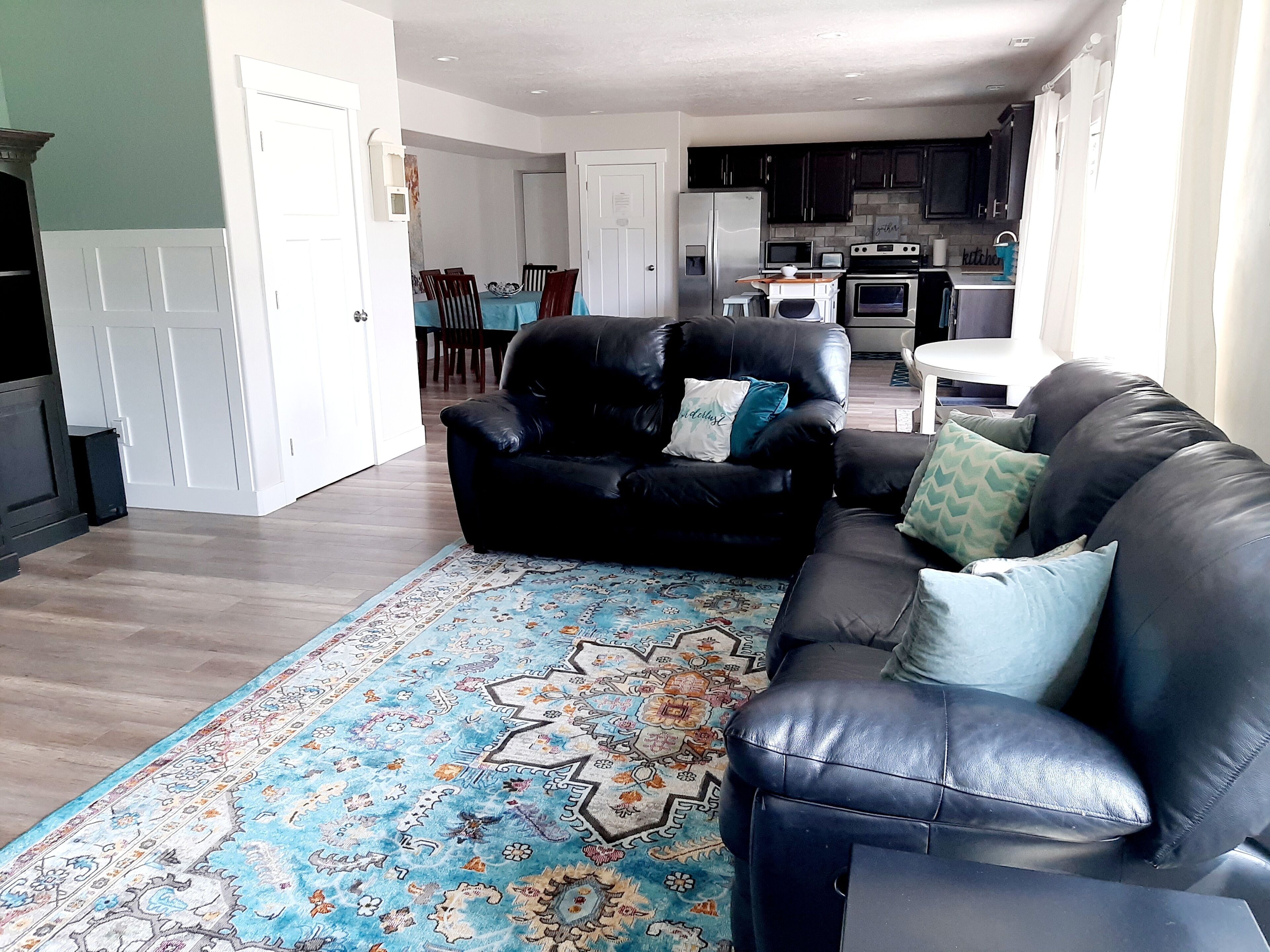 A living room with a black leather sofa, a patterned rug, and a dining area in the background.