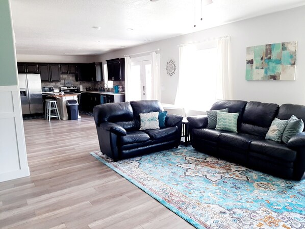 Ein modernes Wohnzimmer mit zwei schwarzen Ledersofas, einem gemusterten Teppich und einer Küche im Hintergrund.