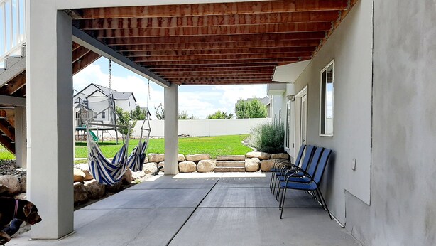 A covered patio area with a concrete floor, a wooden pergola, and several chairs.