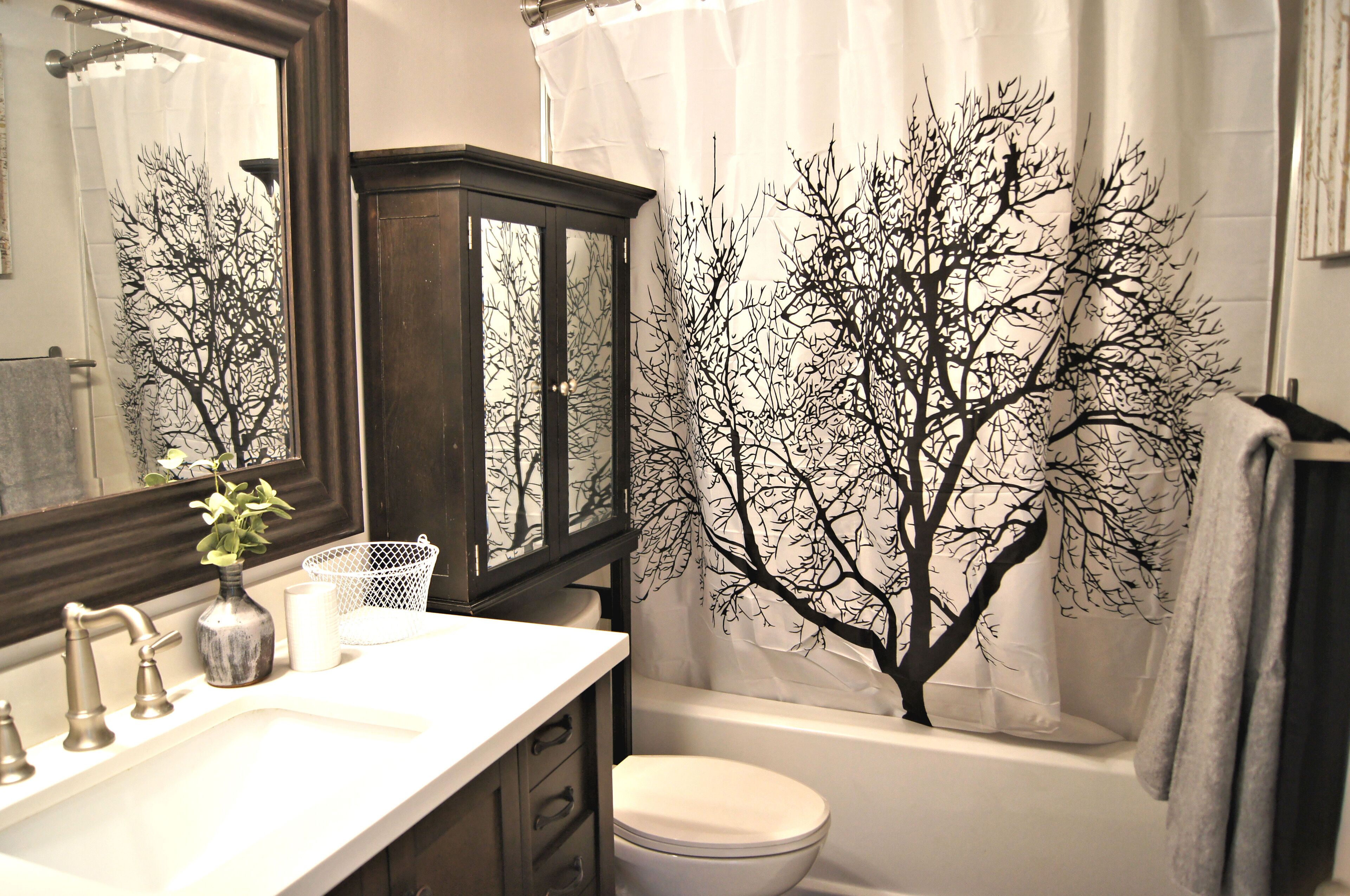 A bathroom with a white sink, a dark wooden cabinet, a white toilet, and a shower curtain with a tree design.