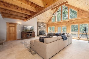 A spacious living room with a high ceiling, large windows, a fireplace, and a cozy seating area. - Loch Nest by Taylor Made Deep Creek (McHenry)