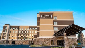 Hotel Staybridge Suites con diseño moderno, destacando una fachada de piedra y un acceso cubierto.