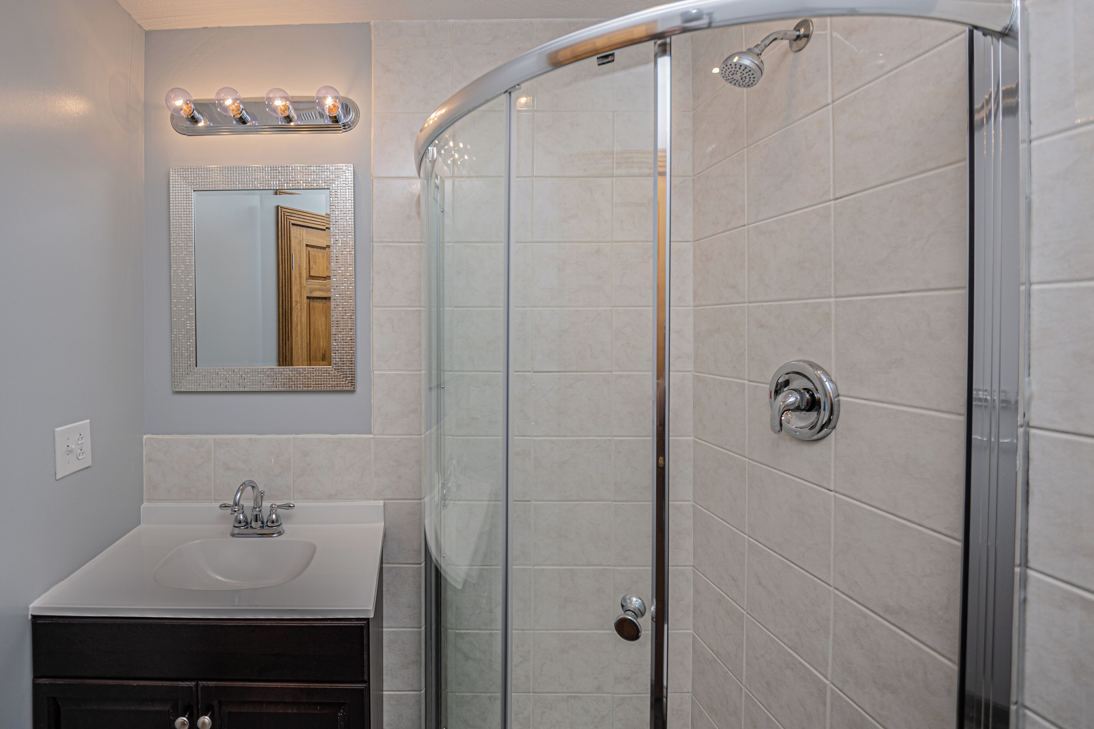 A bathroom with a glass-enclosed shower, a sink with a mirror above it, and a vanity with cabinets.