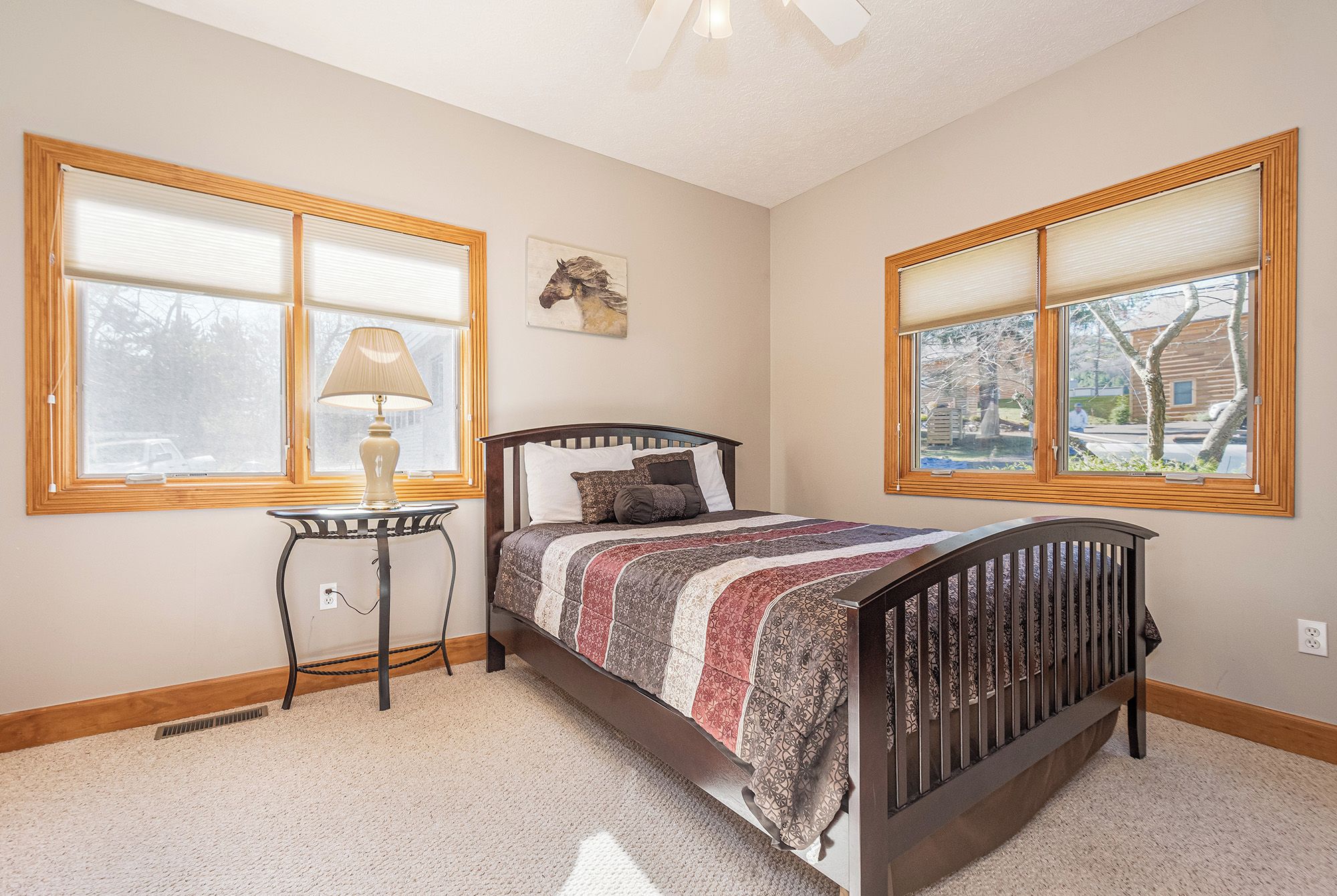 A bedroom with a bed, a nightstand, a lamp, and two windows with blinds.