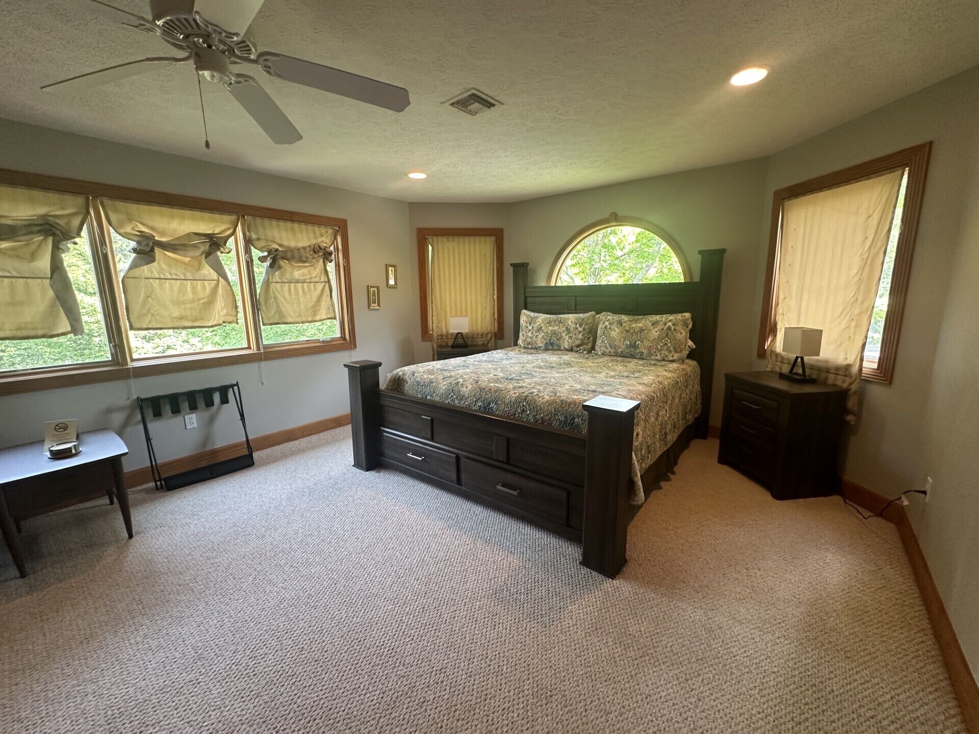 A bedroom with a bed, a desk, a chair, a ceiling fan, and windows with curtains.