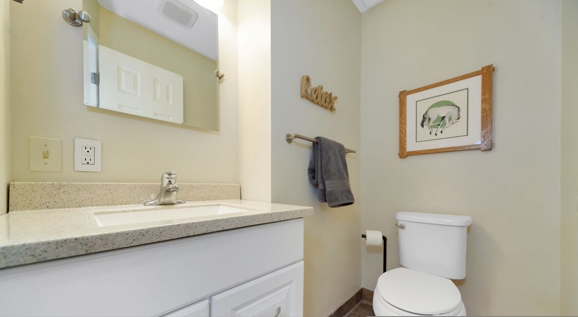 A bathroom with a white sink, mirror, and toilet. There is a towel rack with a towel hanging on it, and a framed picture on the wall.