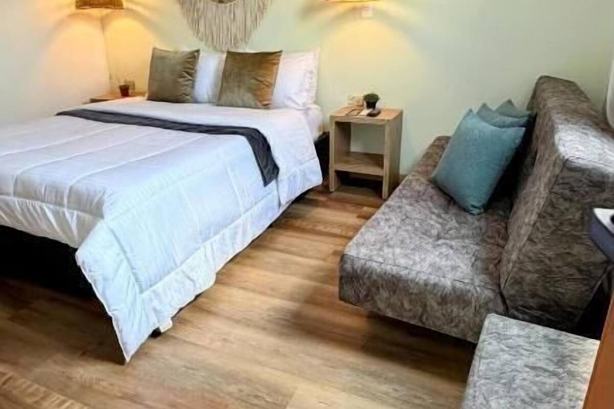 A bedroom with a bed, two bedside tables, a sofa, and two hanging lamps.