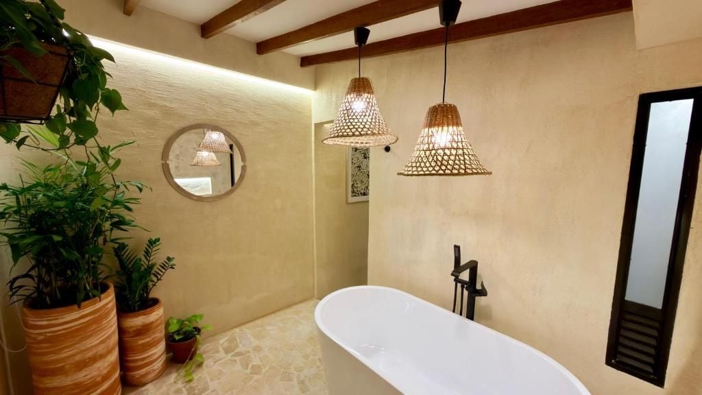 Un baño con una bañera independiente, un espejo redondo e iluminación colgante.