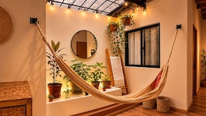 A hammock in a room with wooden flooring, a mirror, and various potted plants. - Luum Guest House (Medellín)