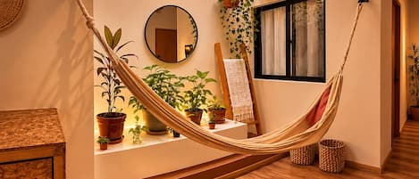 A hammock in a room with wooden flooring, a mirror, and various potted plants.