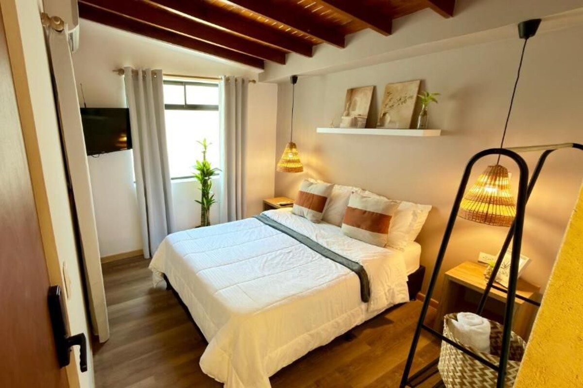 A bedroom with a bed, a bedside table, a hanging lamp, and a window with curtains.