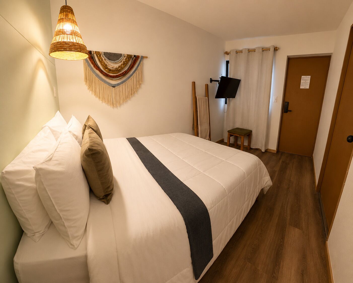 Et hotelværelse med en seng, et fjernsyn, et billede på væggen og en dør.