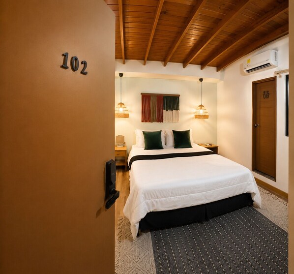 Habitación de hotel con una cama, techo de madera, aire acondicionado de pared y una puerta con un número.