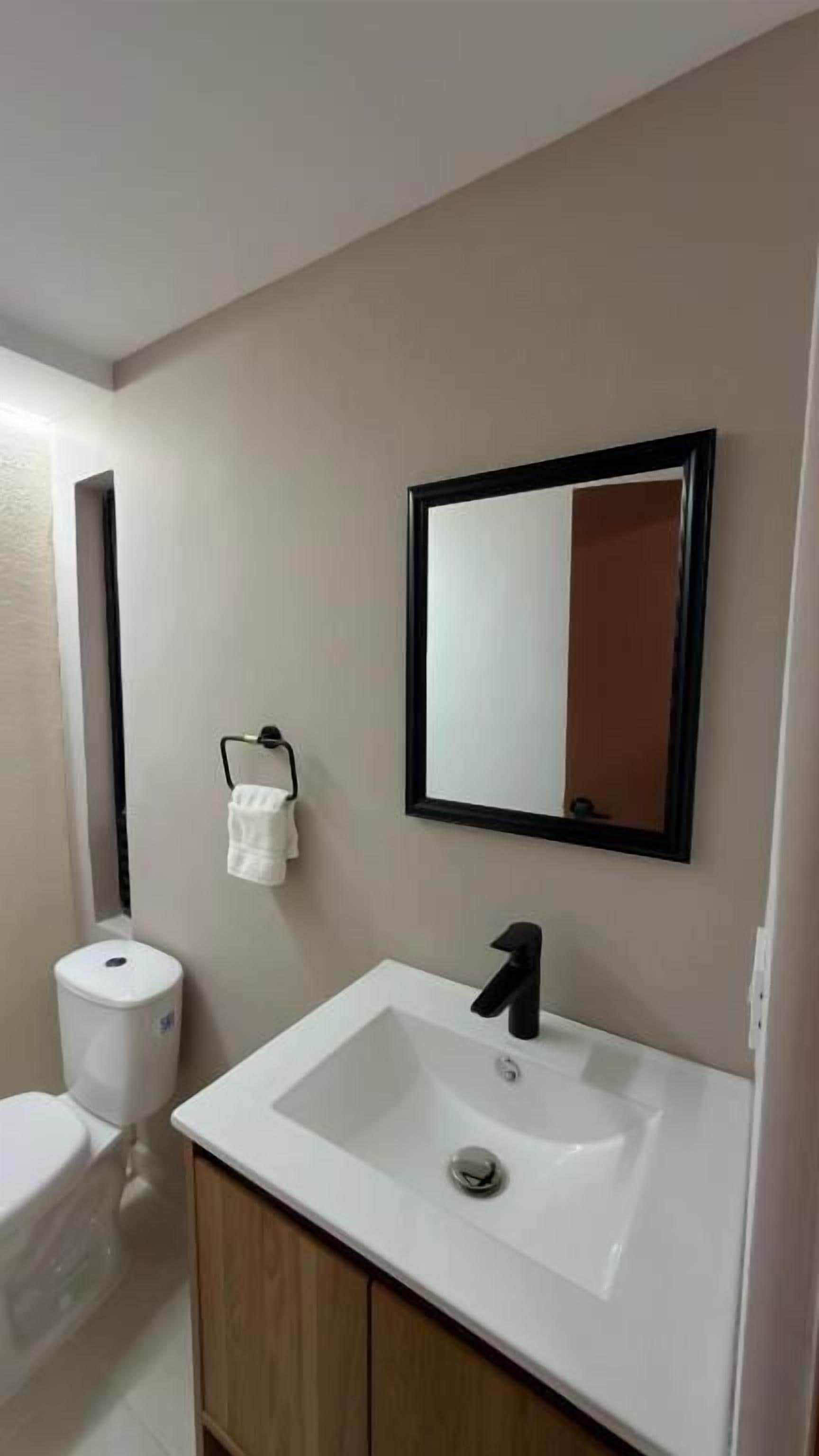 A bathroom with a white sink, a black faucet, a mirror with a black frame, and a toilet.
