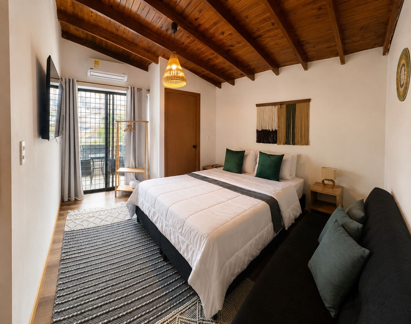 Een slaapkamer met een groot bed, een houten plafond, een klein nachtkastje en uitzicht door een glazen deur.