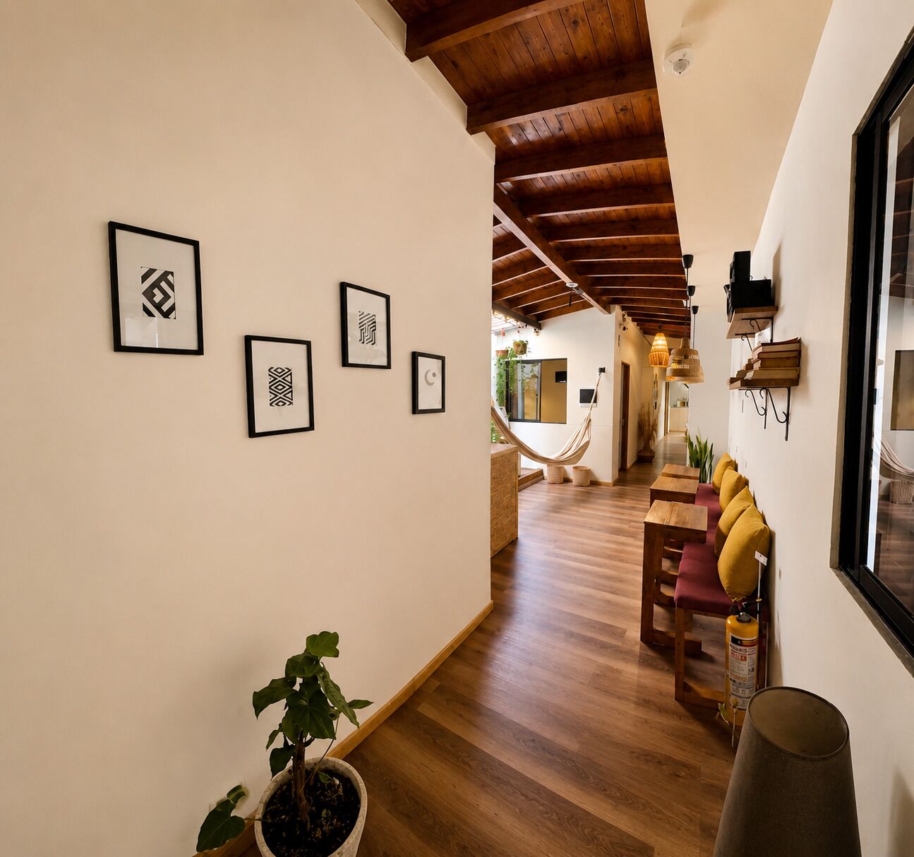 A hallway with wooden flooring, framed artwork on the walls, a hammock, and a seating area with cushions.
