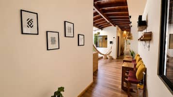 A hallway with wooden flooring, framed artwork on the walls, a hammock, and a seating area with cushions.