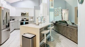 Une cuisine moderne avec des meubles blancs, des appareils en acier inoxydable et un îlot central doté de tabourets.