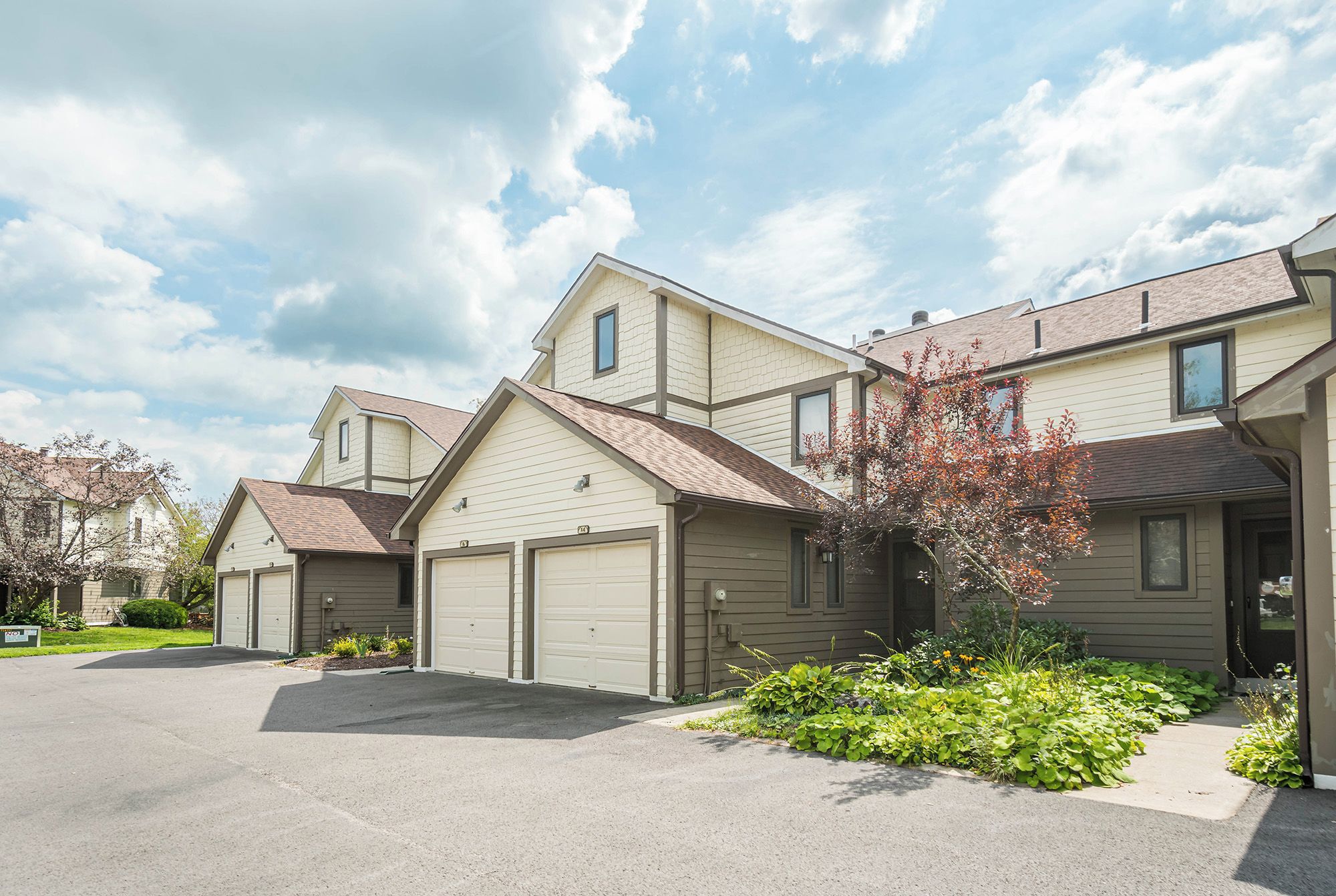 A residential building with two attached garages, a front lawn with a small tree, and a clear sky.