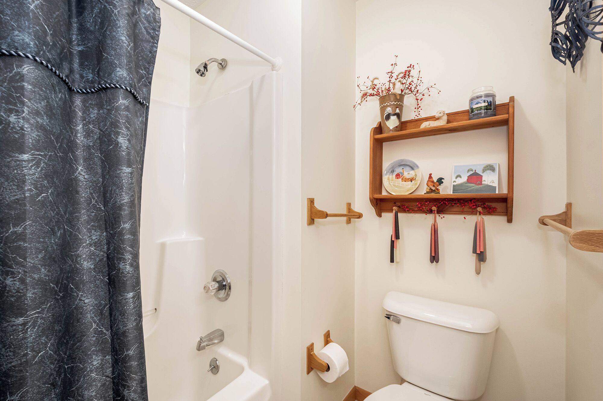 A bathroom with a shower, toilet, and a shelf with decorative items.