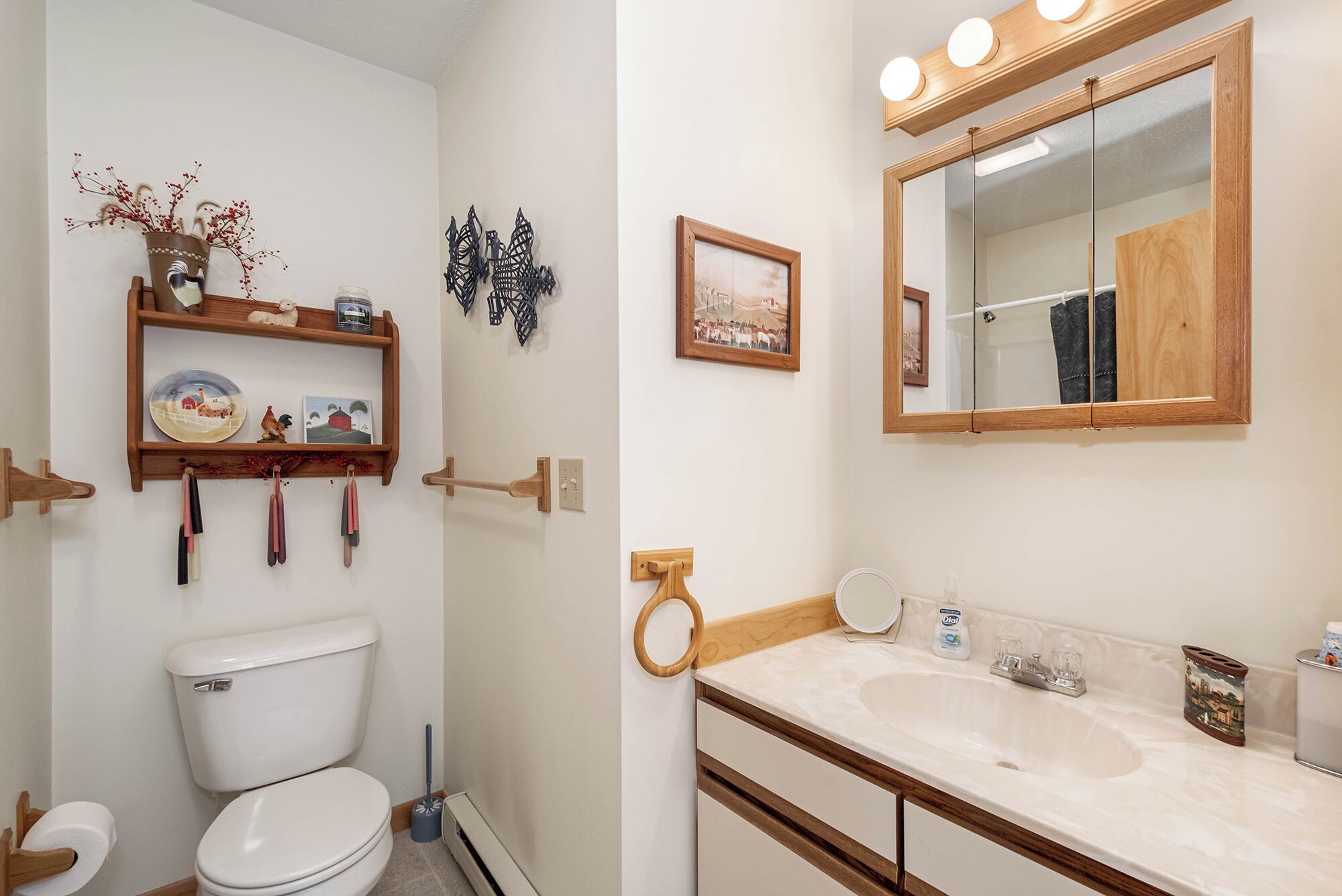 A bathroom with a toilet, a sink with a mirror, and a shelf with decorative items.