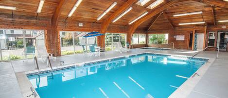 An indoor swimming pool with wooden beams, clear glass walls, and a blue pool.