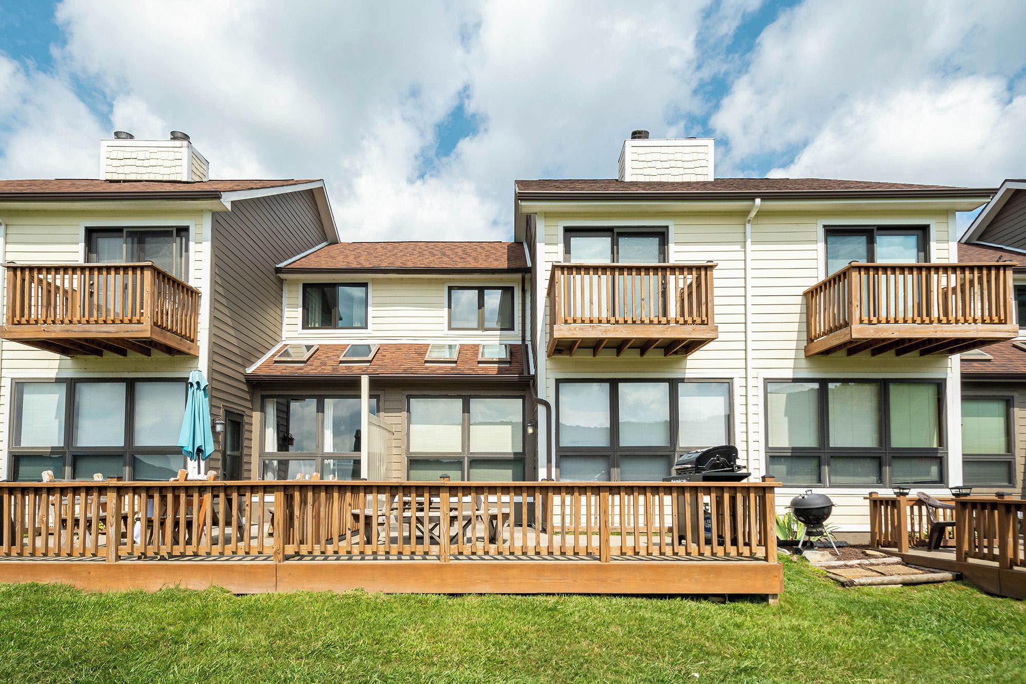 A row of townhouses with balconies, a covered patio, and a grassy lawn.