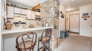A kitchen with a stone wall, wooden chairs, a coffee machine, and a counter with various items. - Ski Harbor 14 by Taylor Made Deep Creek (McHenry)