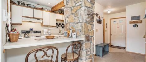 Una cocina con pared de piedra, sillas de madera, una cafetera y una encimera con varios objetos.