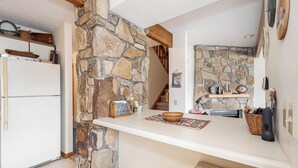 A kitchen with a stone wall, a white countertop, and a refrigerator. - Ski Harbor 14 by Taylor Made Deep Creek (McHenry)