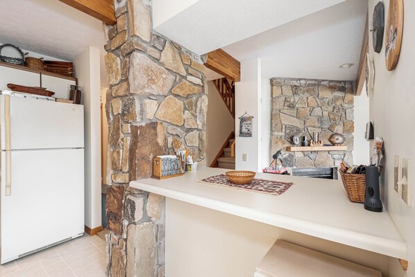 A kitchen with a stone wall, a white countertop, and a refrigerator.
