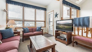 A living room with a sofa, a coffee table, a TV, and a wooden bench. - Ski Harbor 14 by Taylor Made Deep Creek (McHenry)