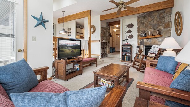 A cozy living room with a television, wooden furniture, a stone fireplace, and a ceiling fan. - Ski Harbor 14 by Taylor Made Deep Creek (McHenry)