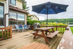 A wooden deck with picnic tables and chairs, a barbecue grill, and a large umbrella.