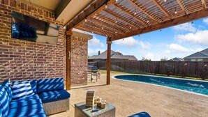 Une terrasse extérieure couverte avec une piscine, un mur en briques et une pergola en bois.