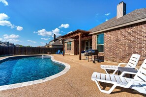 Un jardin avec une piscine, des chaises longues et un espace barbecue.