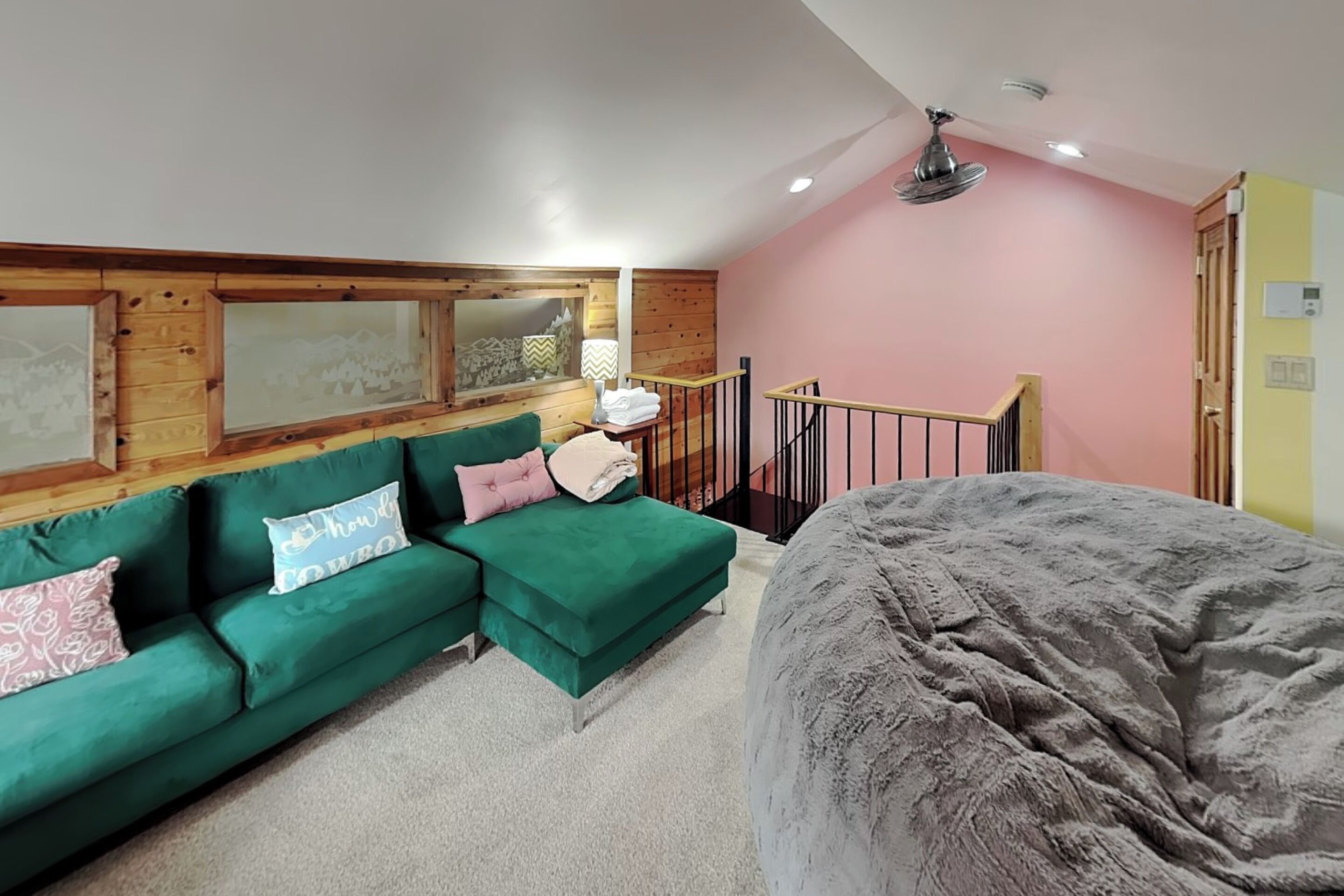 Une pièce avec un canapé vert, un lit, un lambris en bois, une fenêtre donnant sur les montagnes, un ventilateur de plafond et un mur rose.