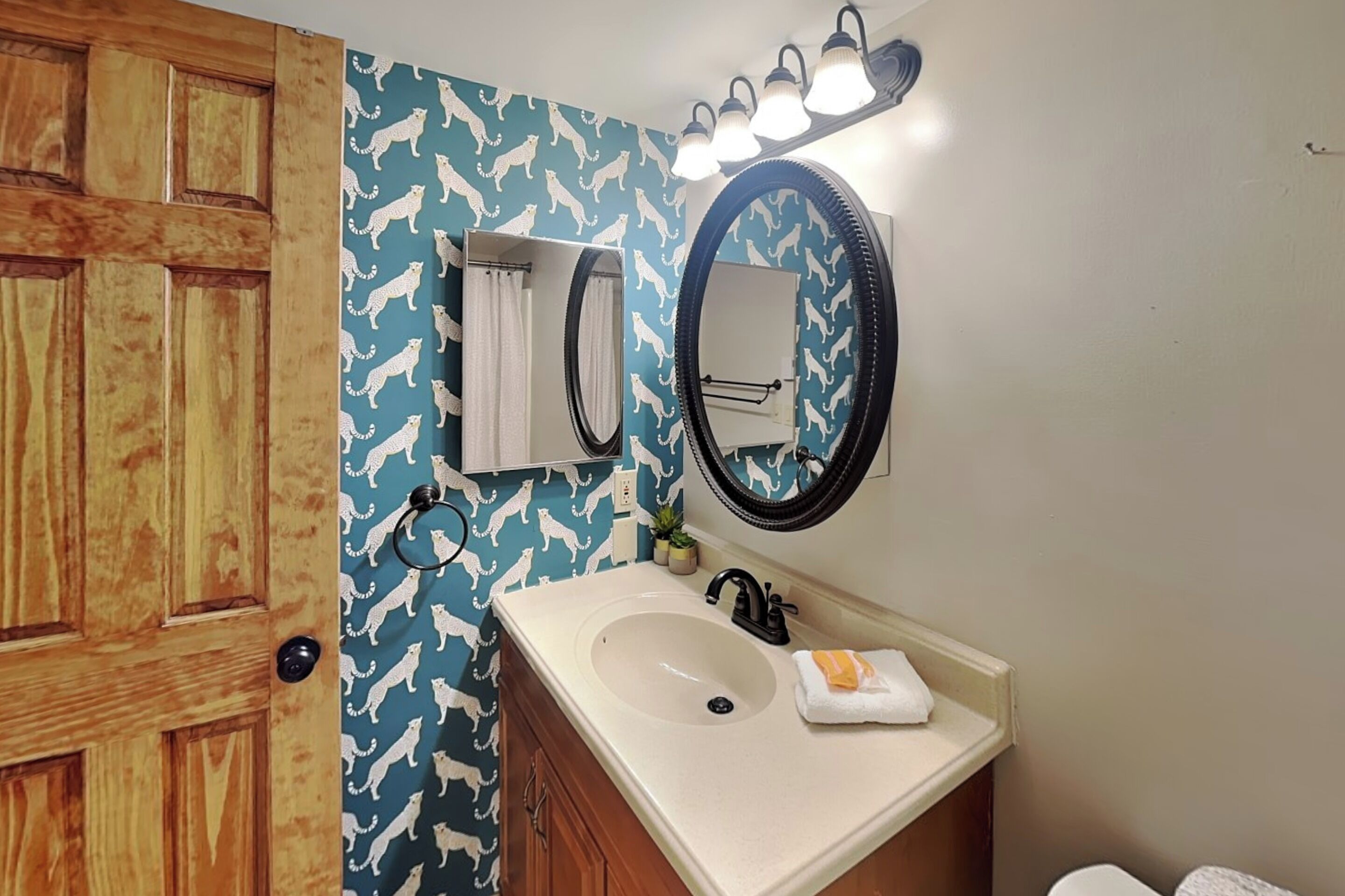 A bathroom with a wooden door, a sink with a towel, and a mirror with lights above.